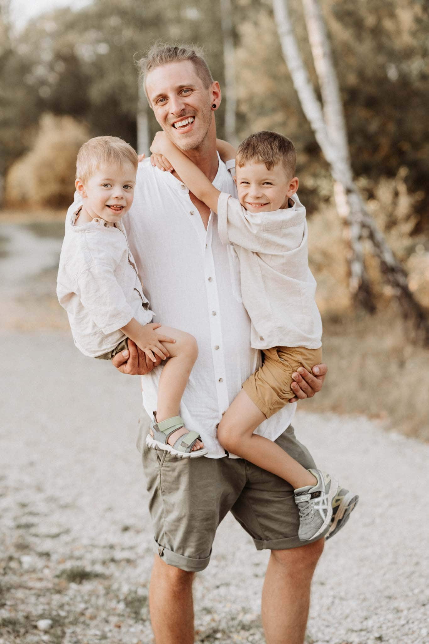 Beim Babybauchshooting hält Papa zwei lachende Kinder am Arm