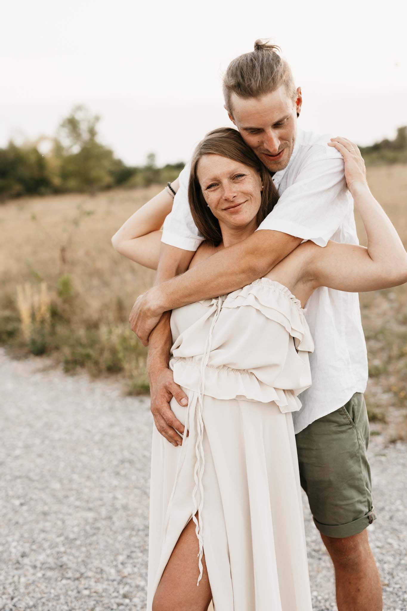 Mann umarmt beim Babybauchshooting seine Schwangere Frau in der Natur