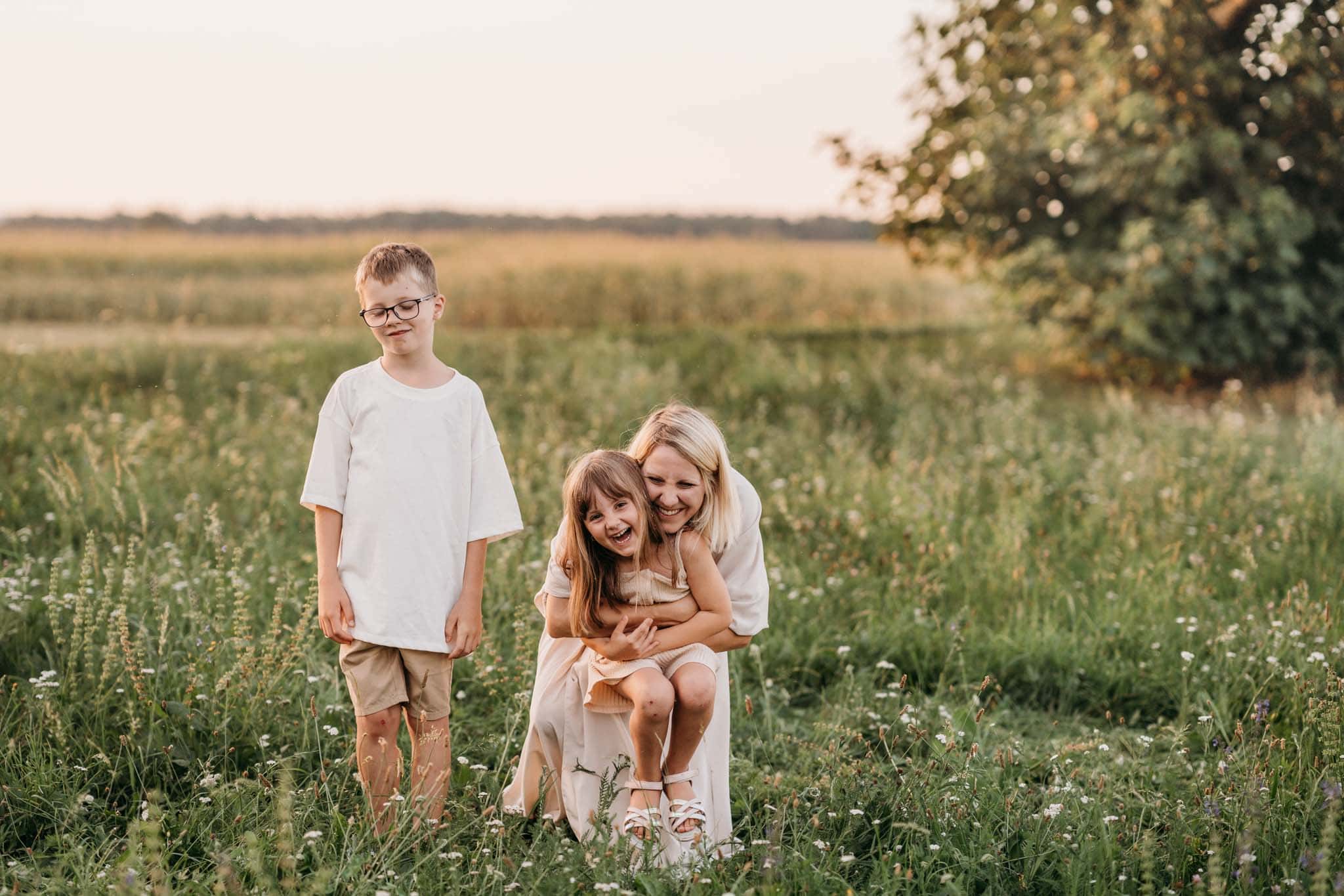 Familienfotografie in München auf Wiese mit Mama und Kindern Mama füngt lachendes Mädchen von hinten