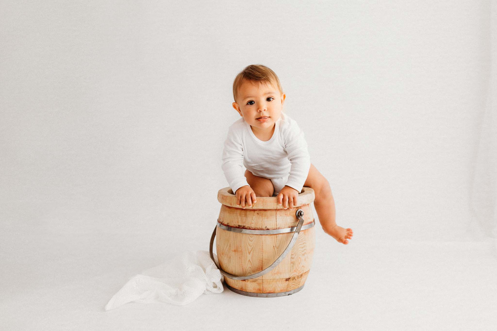 Baby klettert in Holzeimer beim Babyshooting