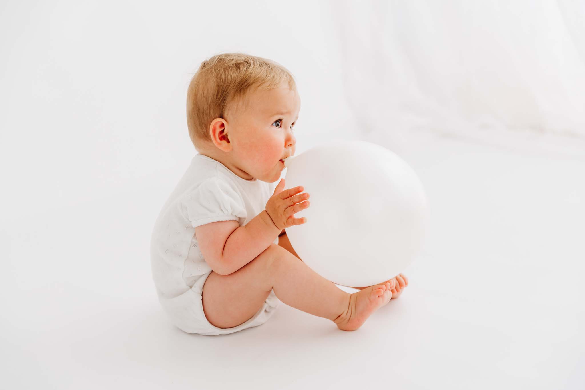 Mädchen bläst weißen Luftballon beim Baby Fotoshooting auf